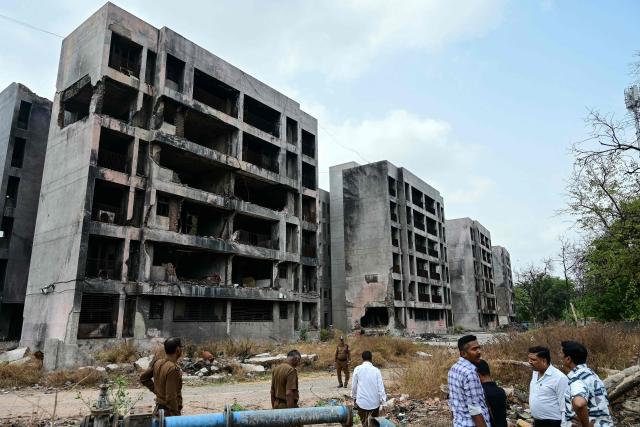 People stand near the damaged residential buildings at a site where Air India flight 171 crashed last year, in Ahmedabad on June 11, 2026. India's aviation accident probe agency is facing renewed criticism from pilot groups ahead of the anniversary of the 2025 Air India Boeing-787 crash in Ahmedabad, which killed 260 people. (Photo by Shammi MEHRA / AFP)