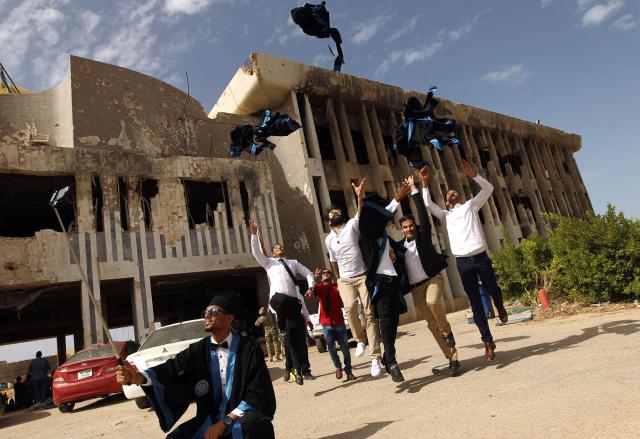 (FILES) Students from the chemical engineering department of Benghazi University throw their academic dresses in the air as they celebrate on October 24, 2016, during their graduation ceremony in front of a building of the university that was destroyed due to fighting. A decade after fierce battles reduced much of the University of Benghazi to rubble, students at Libya's oldest and largest university are once again looking to the future with optimism. The university, founded in 1955, had become after the 2011 uprisings that toppled and killed longtime ruler Muammar Gaddafi the stage of intense fightings between jihadist groups and forces led by military strongman Khalifa Haftar. (Photo by Abdullah DOMA / AFP) / To go with 'Libya-Youth-Development-Education', REPORTAGE by Françoise KADRI