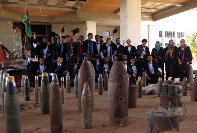 (FILES) Students from the chemical engineering department of Benghazi University pose next to diffused ammunitions and explosive devices on October 24, 2016, during their graduation ceremony outside a building of the university that was destroyed due to fighting. A decade after fierce battles reduced much of the University of Benghazi to rubble, students at Libya's oldest and largest university are once again looking to the future with optimism. The university, founded in 1955, had become after the 2011 uprisings that toppled and killed longtime ruler Muammar Gaddafi the stage of intense fightings between jihadist groups and forces led by military strongman Khalifa Haftar. (Photo by Abdullah DOMA / AFP) / To go with 'Libya-Youth-Development-Education', REPORTAGE by Françoise KADRI