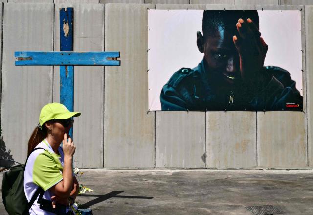A volunteer stands next to a cross and a photograph of a migrant person as Pope Leo XIV meets with organizations working with migrants in the port of Arguineguin on the Canary Island of Gran Canaria, a place accustomed to the arrival of migrants, on June 11, 2026. Pope Leo XIV is visiting Spain June 6-12 with stops in Madrid, Barcelona, and the Canary Islands, where he will meet with migrants and organisations dedicated to helping them. (Photo by Stefano RELLANDINI / AFP)