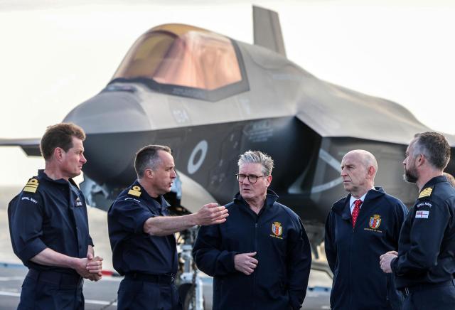 (FILES) Britain's Prime Minister Keir Starmer (C) and Britain's Defence Secretary John Healey (2R) stand in front of an Royal Navy F-35B Lightning fighter jet as they talk with Royal Navy Vice Admiral Andrew Burns (L), Commodore James Blackmore, Captain Will Blackett (R) and Air Wing Commander Captain Colin McGannity (obscured) on the flight deck of the British aircraft carrier HMS Prince Of Wales, in an undisclosed location, on April 24, 2025, following its deployment to the Indo-Pacific region. British Defence Secretary John Healey resigned on June 11, 2026, in a surprise move which he said was due to Prime Minister Keir Starmer and his finance ministry failing to commit sufficient resources to long-term defence plans. (Photo by Richard Pohle / POOL / AFP)