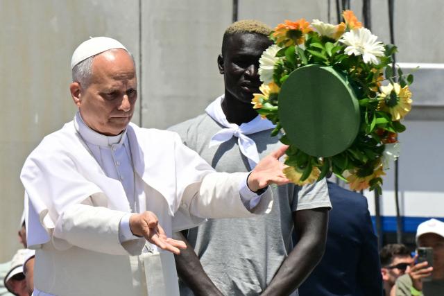 Pope Leo XIV, flanked by two migrants, throws a wreath to the sea to remember all the migrants who perished during their journey, at the Port of Arguineguin on the Canary Island of Gran Canaria, a place accustomed to the arrival of migrants, on June 11, 2026. Pope Leo XIV is visiting Spain June 6-12 with stops in Madrid, Barcelona, and the Canary Islands, where he will meet with migrants and organisations dedicated to helping them. (Photo by Stefano RELLANDINI / AFP)