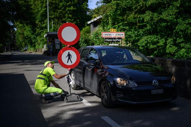 A worker places traffic signs closing the border crossing between Hermance in Switzerland and Chens sur Leman in France, ahead of the upcoming G7 summit in nearby Evian, in Hermance, on June 11, 2026. The closure of 21 of the 28 border crossings between the canton of Geneva and France ahead of the G7 summit is creating a headache for cross-border commuters. (Photo by Fabrice COFFRINI / AFP)