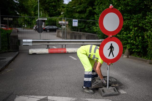 A worker places traffic signs closing the border crossing between Hermance in Switzerland and Chens sur Leman in France, ahead of the upcoming G7 summit in nearby Evian, in Hermance, on June 11, 2026. The closure of 21 of the 28 border crossings between the canton of Geneva and France ahead of the G7 summit is creating a headache for cross-border commuters. (Photo by Fabrice COFFRINI / AFP)