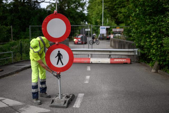 A worker places traffic signs closing the border crossing between Hermance in Switzerland and Chens sur Leman in France, ahead of the upcoming G7 summit in nearby Evian, in Hermance, on June 11, 2026. The closure of 21 of the 28 border crossings between the canton of Geneva and France ahead of the G7 summit is creating a headache for cross-border commuters. (Photo by Fabrice COFFRINI / AFP)