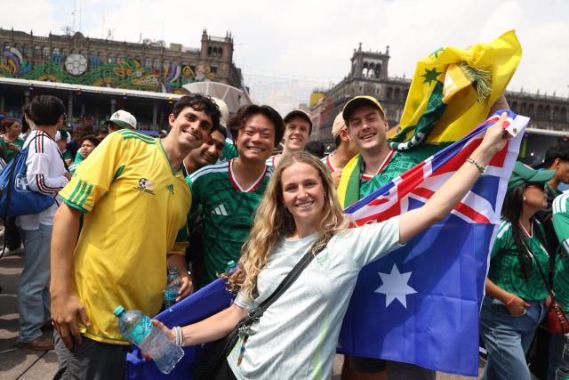 Fans, some wearing Mexico's national team jerseys, pose for a picture holding an Australian flag in the fan zone ahead of the Group A match between Mexico and South Africa at the 2026 FIFA World Cup in Mexico City on June 11, 2026. (Photo by LUIS CORTES / AFP)