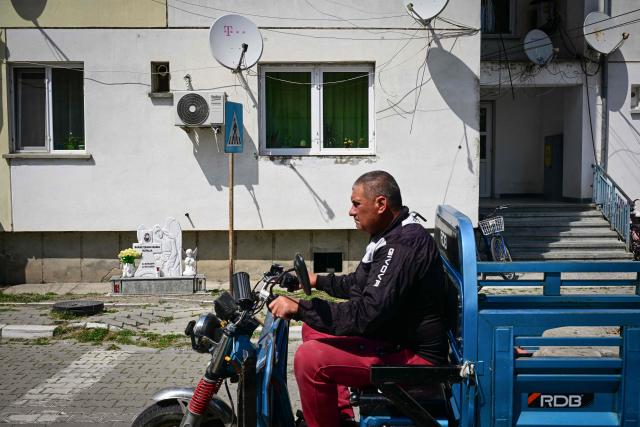 A man drive an electric vehicle next to memorial monument for a child who died in an accident next to a block of flats in Sulina city, Romania, on May 08, 2026. In Sulina, Romania’s easternmost point, Roxana Saraev has decided that anxiety about Russian airstrikes in Ukraine, some kilometres away, won’t make her leave the "oasis of tranquility" she moved to five years ago.In four years of war, the EU and NATO country which shares a 650 km border with Ukraine, has recorded 28 airspace breaches and 47 drone crashes, according to the latest data of the defence ministry. The most serious such incident happened on May 29 in the centre of the city of Galati, 150 km north of Sulina. (Photo by Daniel MIHAILESCU / AFP)