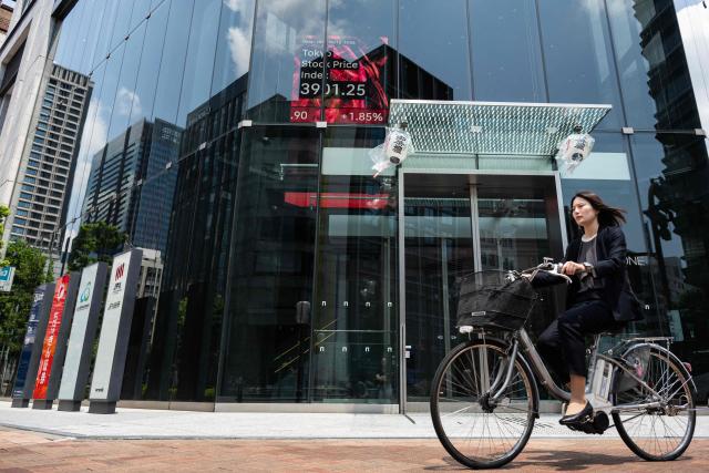 A woman bikes past a building showing an electronic quotation board displaying the Tokyo Stock Exchange in Tokyo on June 12, 2026. Japan's Nikkei share index soared more than four percent on June 12 after US President Donald Trump withdrew his threat of further strikes against Iran and said a deal to end the war could be signed in coming days. (Photo by Andrew CABALLERO-REYNOLDS / AFP)