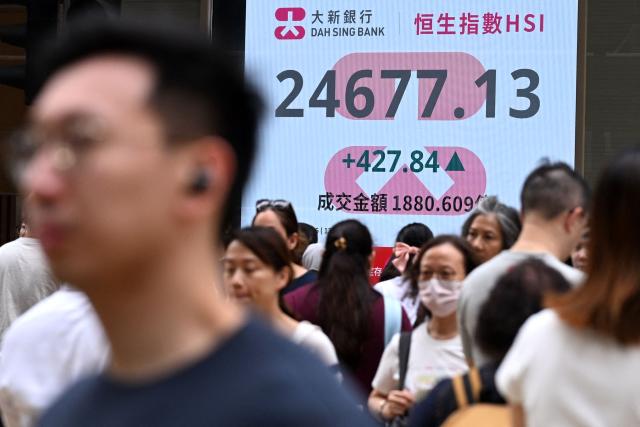 Pedestrians walk across a street next to an electronic sign board showing the Hang Seng Index in Hong Kong on June 12, 2026. (Photo by Peter PARKS / AFP)