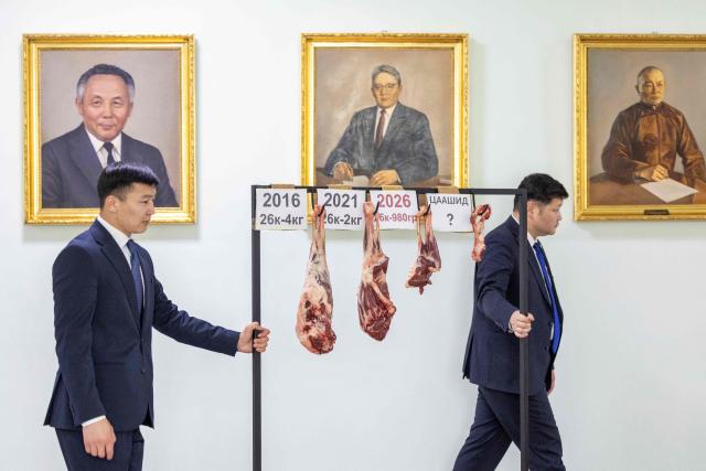 TOPSHOT - Democratic Party members Batmunkh Davaasambuu (L) and Enkhmunkh Batjargal push a display of sheep meat past portraits of former Mongolian prime ministers in the corridor of the State Palace in Ulaanbaatar, the capital of Mongolia, on June 11, 2026. Members of the Democratic Party held a briefing for media using sheep meat to highlight price increases over the past 10 years and demanded accountability from the ruling Mongolian People’s Party. (Photo by BYAMBASUREN BYAMBA-OCHIR / AFP)