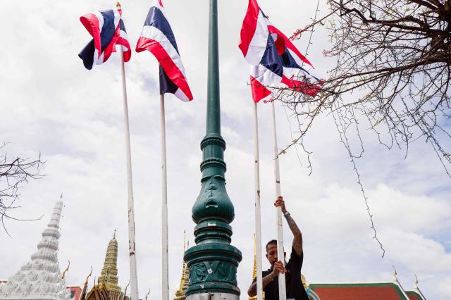A worker displays flagpoles with Thailand’s national flag on a pavement opposite the main entrance gate to the Grand Palace complex in Bangkok on June 12, 2026. Thai Princess Bajrakitiyabha Mahidol, the king's eldest daughter, has died aged 47, the royal palace announced on June 12, more than three years after she was hospitalised following a sudden illness. (Photo by ANTHONY WALLACE / AFP)