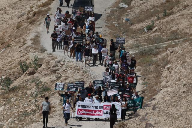 Palestinians and Israeli left-wing activists hold placards during their protest march against the planned eviction of the villagers at Khan al-Ahmar in the Israeli-occupied West Bank on June 12, 2026. Excluding east Jerusalem, more than 500,000 Israelis live in settlements in the West Bank, which Israel has occupied since 1967, among some three million Palestinians. (Photo by Ahmad GHARABLI / AFP)