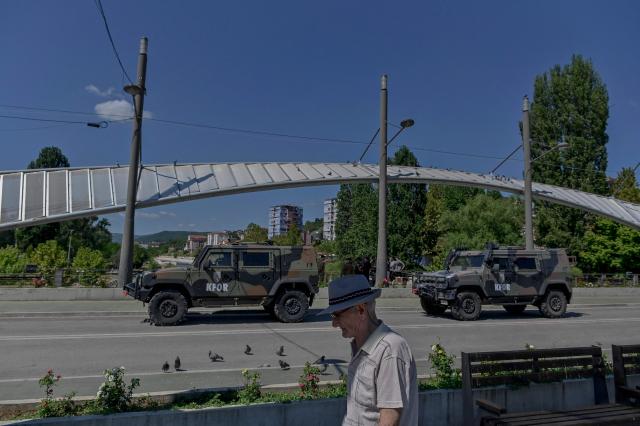 (FILES) A man walks as members of the KFOR - NATO led peacekeeping mission in Kosovo patrol over the main bridge in Mitrovica on August 10, 2024. NATO announced on June 12, 2026 that it was reducing the size of its military mission in Kosovo, KFOR, due to the “improvement” in security conditions in the small Balkan country. (Photo by Armend NIMANI / AFP)