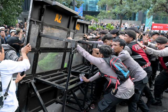 Students and police officers struggle over the barricades blocking their path as they demonstrated to demand a reduction in fuel prices and the dissolution of the free meal program, which they consider to be a hotbed of corruption, in Jakarta on June 12, 2026. (Photo by BAY ISMOYO / AFP)