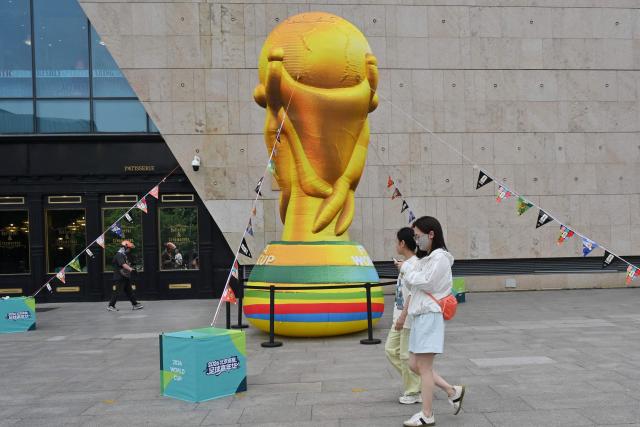 People walk past an effigy featuring the World Cup trophy at a shopping center in Beijing on June 12, 2026. (Photo by ADEK BERRY / AFP)
