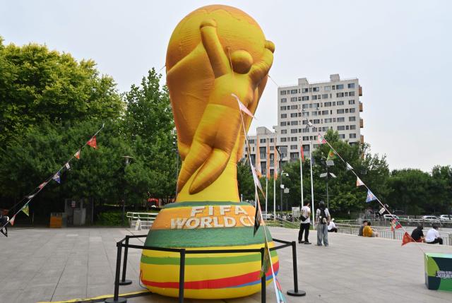 People walk past an effigy featuring the World Cup trophy at a shopping center in Beijing on June 12, 2026. (Photo by ADEK BERRY / AFP)