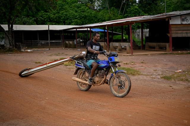 A miner rides a motorcycle carrying a sheet of zinc as he leaves an artisanal gold mine in Las Brisas de Cuyuni,  near the town of Las Claritas, Bolivar state, Venezuela, on June 11, 2026. Venezuela, home to the world's largest oil reserves, also has deposits of gold, diamonds, bauxite, coltan and rare earths, but much of its mining areas — notably the 112,000 sq km Mining Arc located in remote regions far from major cities — is controlled by armed gangs or guerrilla groups. (Photo by Federico PARRA / AFP)