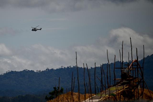 A Venezuelan army helicopter flies over Las Brisas de Cuyuni, as seen from an artisanal gold mine near the town of Las Claritas in Bolivar state, Venezuela, during a security operation on June 11, 2026. Venezuela, home to the world's largest oil reserves, also has deposits of gold, diamonds, bauxite, coltan and rare earths, but much of its mining areas — notably the 112,000 sq km Mining Arc located in remote regions far from major cities — is controlled by armed gangs or guerrilla groups. (Photo by Federico PARRA / AFP)