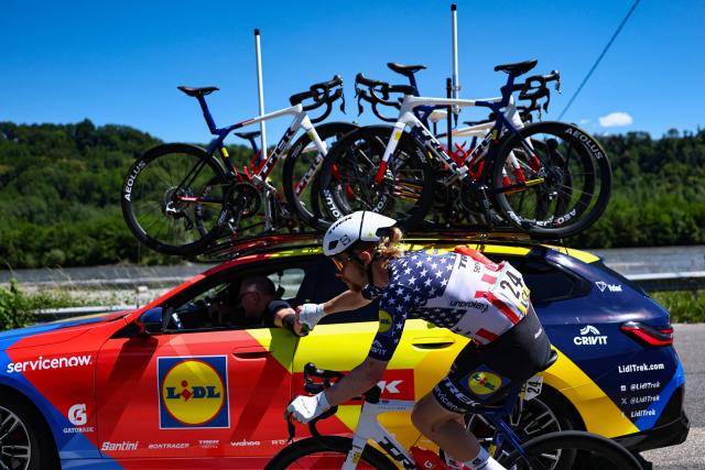 Lidl-Trek's US rider Quinn Simmons grabs a hydration bottle from his team vehicle as he cycles during the 6th stage of the Tour Auvergne-Rhone-Alpes cycling race (formerly known as the Criterium du Dauphine), 182,3km between Saint-Vulbas and Crest-Voland in the French Alps on June 12, 2026. (Photo by Anne-Christine POUJOULAT / AFP)