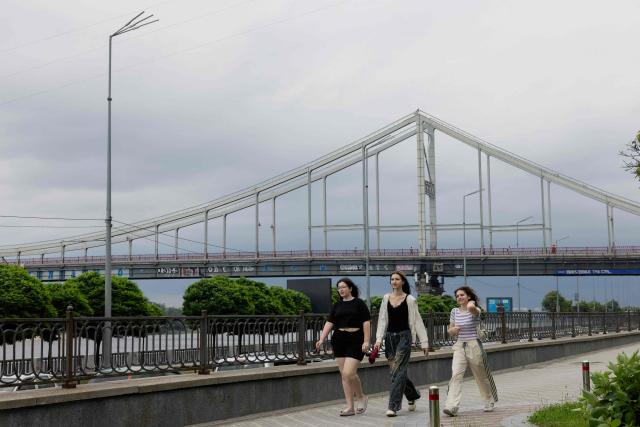 A group of girls walk down the street along the Dnipro River before the rain falls in Kyiv on June 12, 2026, amid the Russian invasion of Ukraine. (Photo by Tetiana DZHAFAROVA / AFP)