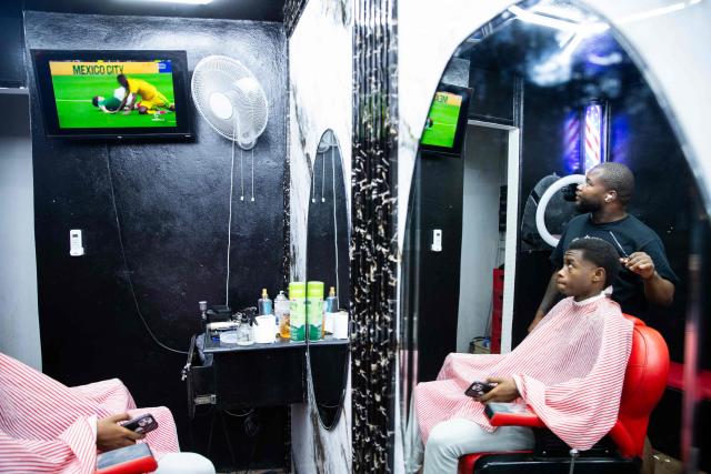 This photo taken on June 11, 2026 shows people in a barber shop watching the opening match of the 2026 World Cup football tournament between Mexico and South Africa on a television in Port-au-Prince, Haiti. The 2026 World Cup football tournament kicked off in Mexico City on June 11. (Photo by Clarens SIFFROY / AFP)