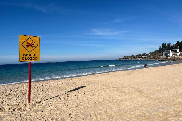 A beach closed sign is displayed at Coogee Beach in Sydney on June 13, 2026. Beachgoers dragged a badly injured swimmer from the water at Coogee, one of Australia's most beloved beaches and popular spot for tourists, after she was mauled by a shark on June 13, police said. Four people have been killed in an unusual spate of shark attacks around Australia this year. (Photo by OLIVER HOTHAM / AFP)