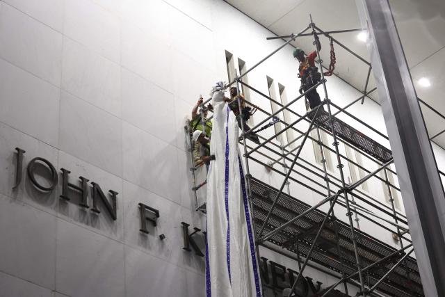 Workers hang a flame retardant tarp on scaffolding near the signage for the "Donald J. Trump and John F. Kennedy Memorial Center for the Performing Arts" in Washington, DC, early on June 13, 2026. A US federal judge on June 12 rejected a bid by the board of the Kennedy Center and the Justice Department to halt the removal of President Donald Trump's name from the performing arts venue. District Judge Christopher Cooper, in a ruling last month, ordered Trump's name taken off the iconic building in the nation's capital by Friday, June 12, 2026. (Photo by Alex WROBLEWSKI / AFP)