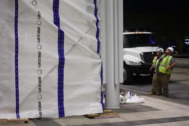Workers hang a flame retardant tarp on scaffolding near the signage for the "Donald J. Trump and John F. Kennedy Memorial Center for the Performing Arts" in Washington, DC, early on June 13, 2026. A US federal judge on June 12 rejected a bid by the board of the Kennedy Center and the Justice Department to halt the removal of President Donald Trump's name from the performing arts venue. District Judge Christopher Cooper, in a ruling last month, ordered Trump's name taken off the iconic building in the nation's capital by Friday, June 12, 2026. (Photo by Alex WROBLEWSKI / AFP)