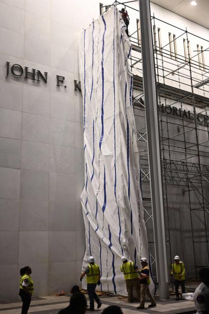Workers hang a flame retardant tarp on scaffolding near the signage for the "Donald J. Trump and John F. Kennedy Memorial Center for the Performing Arts" in Washington, DC, early on June 13, 2026. A US federal judge on June 12 rejected a bid by the board of the Kennedy Center and the Justice Department to halt the removal of President Donald Trump's name from the performing arts venue. District Judge Christopher Cooper, in a ruling last month, ordered Trump's name taken off the iconic building in the nation's capital by Friday, June 12, 2026. (Photo by Alex WROBLEWSKI / AFP)