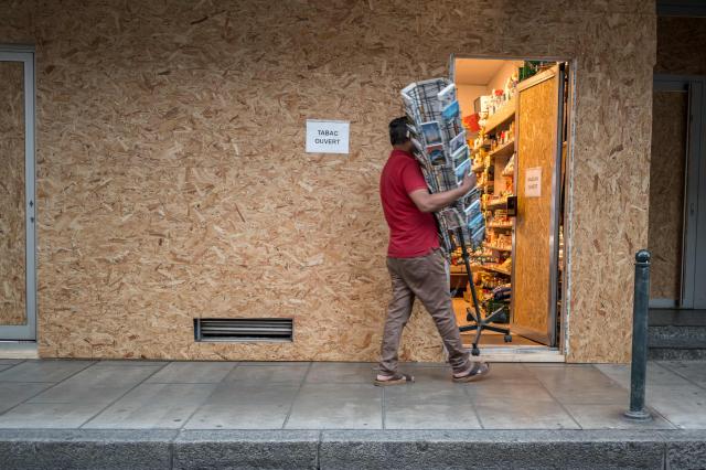 A vendor brings a postcard display stand inside his shop, which is boarded up with wooden panels to protect the façade ahead of demonstrations against the nearby G7 summit in Évian, in Geneva, June 12, 2026. Protests against the G7 summit in Evian are set to take place in nearby Geneva, where activists can gather more easily than in the tightly secured host town. (Photo by Fabrice COFFRINI / AFP)