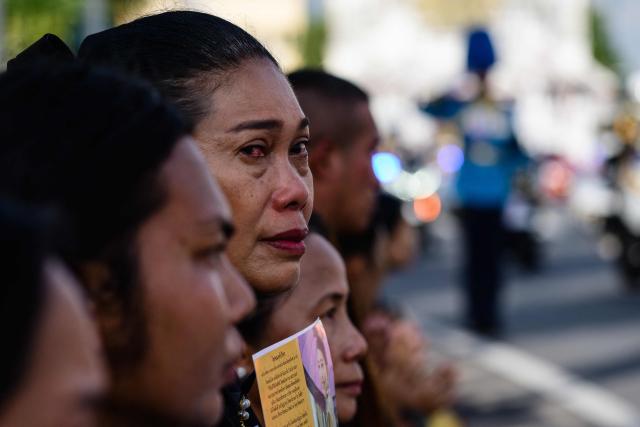 Mourners react as the hearse carrying the body of Thai Princess Bajrakitiyabha Mahidol drives past, outside the Grand Palace, where funeral rites will begin for the late princess, in Bangkok on June 13, 2026. Hundreds of black-clad Thai mourners gathered at the royal palace in Bangkok on June 13, awaiting the arrival of the body of the king's eldest daughter a day after her death was announced. (Photo by ANTHONY WALLACE / AFP)