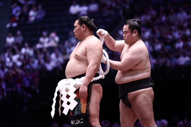 A Sumo wrestler helps Mongolian-born Hoshoryu, who holds the highest rank of Yokozuna (grand champion), (L) to tie his belt on day 1 of the 2026 MUFG Paris Sumo Tournament, in Paris on June 13, 2026. (Photo by Behrouz MEHRI / AFP)