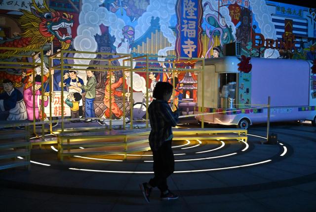 A woman walks past murals at a shopping center in Beijing on June 13, 2026. (Photo by ADEK BERRY / AFP)