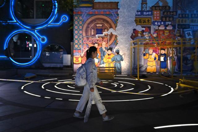 A woman walks past murals at a shopping center in Beijing on June 13, 2026. (Photo by ADEK BERRY / AFP)