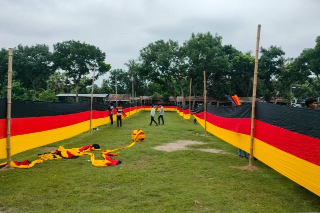 People look at a 7.5 kilometres (4.7 miles) long national flag of Germany commisioned by their football team fan Bangladeshi farmer Amjad Hossain, upon its display across a field in Magura district on June 10, 2026, on the eve of the 2026 FIFA World Cup tournament. Across Bangladesh, football fans have decked out their rooftops with the flags of Brazil and Argentina -- the most popular teams in a country that has never qualified for the World Cup. However, one man stands out not only for choosing a less-favoured team, but also for the sheer strength of his support. (Photo by AFP)