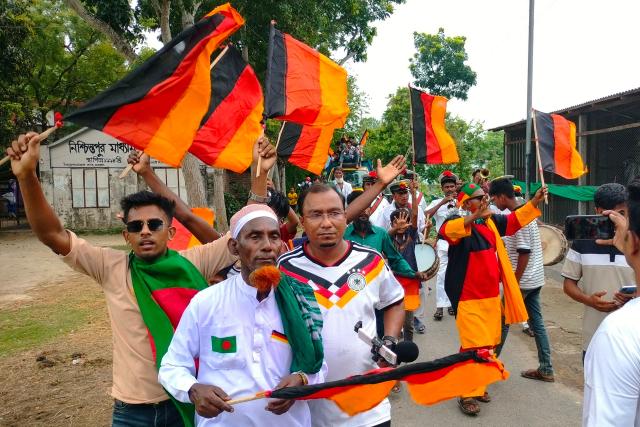 Football fans attend the unveiling of Germany's 7.5 kilometres (4.7 miles)-long national flag commisioned by Bangladeshi farmer Amjad Hossain (2L) in Magura district on June 10, 2026, on the eve of the 2026 FIFA World Cup tournament. Across Bangladesh, football fans have decked out their rooftops with the flags of Brazil and Argentina -- the most popular teams in a country that has never qualified for the World Cup. However, one man stands out not only for choosing a less-favoured team, but also for the sheer strength of his support. (Photo by AFP)