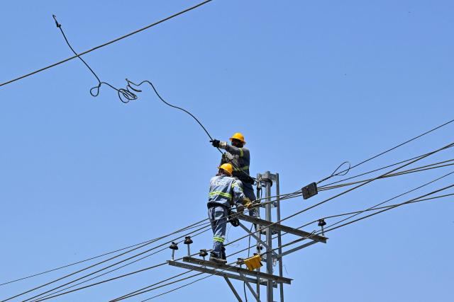 Electricians work on high-voltage power lines in Lahore on June 14, 2026. (Photo by Arif ALI / AFP)