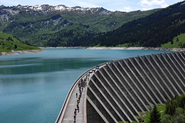 The pack of riders (peloton) cycles over the Barrage de Roselend during the 8th and final stage of the Tour Auvergne-Rhone-Alpes cycling race (formerly known as the Criterium du Dauphine), 120,1km between Beaufort and Plateau de Solaison, in the French Alps on June 14, 2026. (Photo by Anne-Christine POUJOULAT / AFP)