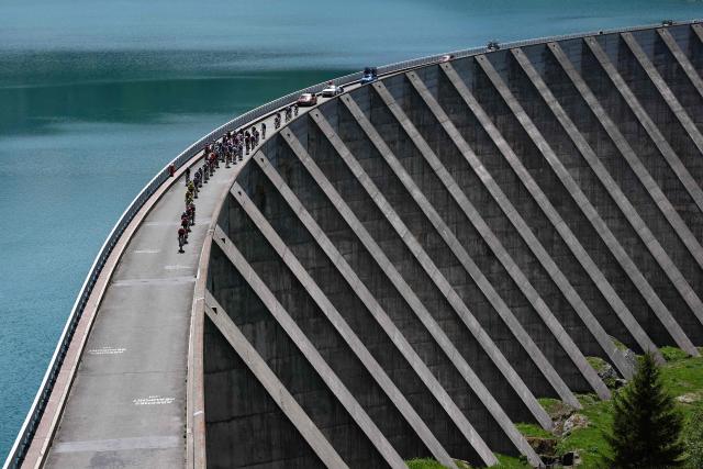 The pack of riders (peloton) cycles over the Barrage de Roselend during the 8th and final stage of the Tour Auvergne-Rhone-Alpes cycling race (formerly known as the Criterium du Dauphine), 120,1km between Beaufort and Plateau de Solaison, in the French Alps on June 14, 2026. (Photo by Anne-Christine POUJOULAT / AFP)