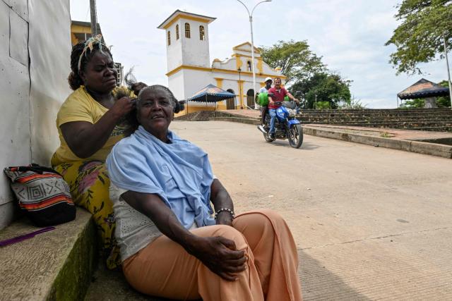 A woman braids another woman's hair near the Buenos Aires police station, months after it was heavily attacked, in Buenos Aires, Cauca department, Colombia, on June 13, 2026. Colombia will hold the runoff presidential election on June 21. (Photo by JOAQUIN SARMIENTO / AFP)