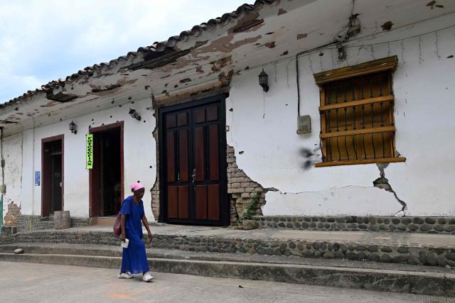 A woman walks past a facade riddled with bullet holes near the Buenos Aires police station, months after it was heavily attacked, in Buenos Aires, Cauca department, Colombia, on June 13, 2026. Colombia will hold the runoff presidential election on June 21. (Photo by JOAQUIN SARMIENTO / AFP)
