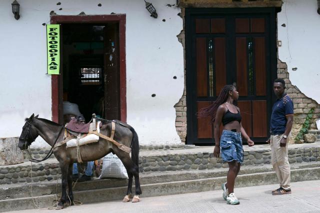 A horse and people are seen in front of a facade riddled with bullet holes near the Buenos Aires police station, months after it was heavily attacked, in Buenos Aires, Cauca department, Colombia, on June 13, 2026. Colombia will hold the runoff presidential election on June 21. (Photo by JOAQUIN SARMIENTO / AFP)