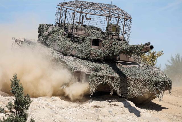 French soldiers stand guard in front of a AMX Leclerc (Char Leclerc) battle tank with an anti-drone cage in its top during a dynamic demonstration of military equipment at the Eurosatory trade show, dedicated to defense and security, at the Paris Nord Villepinte Exhibition Center in Villepinte, northeastern suburb of Paris on June 14, 2026. The Eurosatory trade show takes place from June 15 to 19, 2026. (Photo by Kenzo TRIBOUILLARD / AFP)