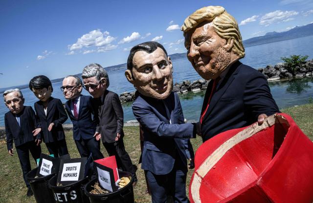 Demonstrators dressed up with caricature "big heads" representing the G7 heads of state (from L) Prime Minister of Canada Mark Carney, Prime Minister of Japan Sanae Takaichi, Chancellor of Germany Friedrich Merz, Prime Minister of the United Kingdom Keir Starmer,  France's President Emmanuel Macron and US President Donald Trump, pose in front of mock trash cans with "human rights, "gender equality" and "climate" placards inside during a happening organised by the NGO OXFAM, in Publier eastern France, on June 14, 2026. A G7 summit is set to take place June 15 to 17 in the French town of Evian-les-Bains near Switzerland and it will be attended by country leaders as well as the EU's foreign policy chief and ministers from Brazil, Canada, the United Arab Emirates and Turkey. (Photo by JEFF PACHOUD / AFP)