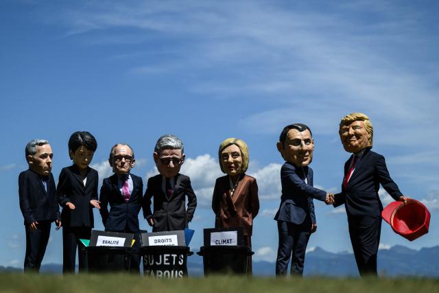 Demonstrators dressed up with caricature "big heads" representing the G7 heads of state (from L) Prime Minister of Canada Mark Carney, Prime Minister of Japan Sanae Takaichi, Chancellor of Germany Friedrich Merz, Prime Minister of the United Kingdom Keir Starmer,  France's President Emmanuel Macron and US President Donald Trump, pose in front of mock trash cans with "human rights, "gender equality" and "climate" placards inside during a happening organised by the NGO OXFAM, in Publier eastern France, on June 14, 2026. A G7 summit is set to take place June 15 to 17 in the French town of Evian-les-Bains near Switzerland and it will be attended by country leaders as well as the EU's foreign policy chief and ministers from Brazil, Canada, the United Arab Emirates and Turkey. (Photo by JEFF PACHOUD / AFP)