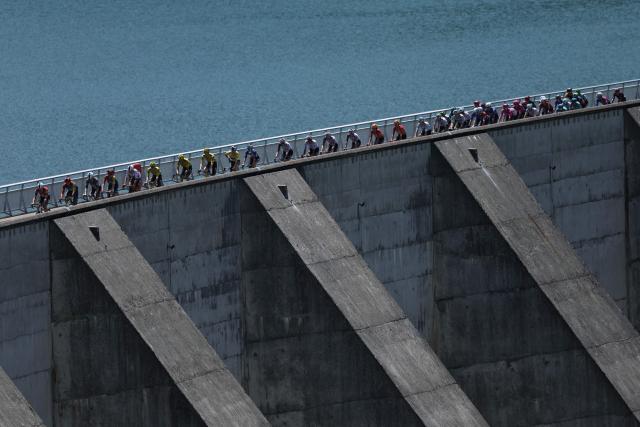 The pack of riders (peloton) cycles over the Barrage de Roselend during the 8th and final stage of the Tour Auvergne-Rhone-Alpes cycling race (formerly known as the Criterium du Dauphine), 120,1km between Beaufort and Plateau de Solaison, in the French Alps on June 14, 2026. (Photo by Anne-Christine POUJOULAT / AFP)