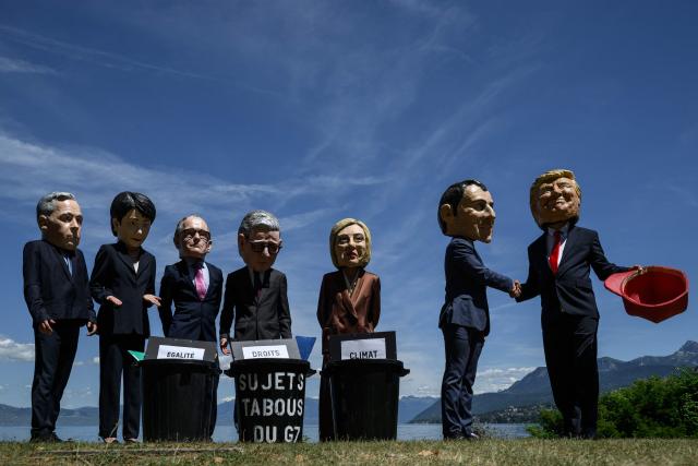 Demonstrators dressed up with caricature "big heads" representing the G7 heads of state (from L) Prime Minister of Canada Mark Carney, Prime Minister of Japan Sanae Takaichi, Chancellor of Germany Friedrich Merz, Prime Minister of the United Kingdom Keir Starmer, Prime Minister of Italy Giorgia Meloni, France's President Emmanuel Macron and US President Donald Trump, pose in front of mock trash cans with "human rights, "gender equality" and "climate" placards inside during a happening organised by the NGO OXFAM, in Publier eastern France, on June 14, 2026. A G7 summit is set to take place June 15 to 17 in the French town of Evian-les-Bains near Switzerland and it will be attended by country leaders as well as the EU's foreign policy chief and ministers from Brazil, Canada, the United Arab Emirates and Turkey. (Photo by JEFF PACHOUD / AFP)