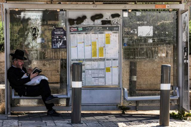 An Israeli Orthodox Jewish man reads a book as he sits at a bus station in near the Jaffa Gate of the old city of Jerusalem on June 14, 2026. (Photo by HAZEM BADER / AFP)