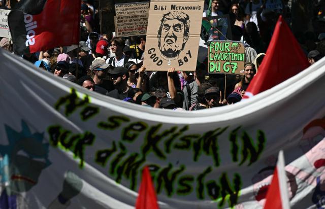 Demonstrators with placards, including one (C) depicting US President Donald Trump and reading "Bibi Netanyahu's good boy" take part in a rally of a "No-G7" coalition of over 60 associations, unions and left-wing groups "against fascism and imperialism, a day ahead of the summit's start, in Geneva on June 14, 2026. The 2026 edition of the G7 summit is set to take place June 15 to 17 in the French town of Evian-les-Bains near Switzerland, attended by country leaders as well as the EU's foreign policy chief and ministers from Brazil, Canada, the United Arab Emirates and Turkey. (Photo by Fabrice COFFRINI / AFP)