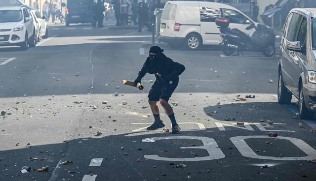 A demonstrator holds wine bottles and a piece of wood amid broken glass and other debris on a street during a rally of a "No-G7" coalition of over 60 associations, unions and left-wing groups "against fascism and imperialism, a day ahead of the summit's start, in Geneva on June 14, 2026. The 2026 edition of the G7 summit is set to take place June 15 to 17 in the French town of Evian-les-Bains near Switzerland, attended by country leaders as well as the EU's foreign policy chief and ministers from Brazil, Canada, the United Arab Emirates and Turkey. (Photo by Fabrice COFFRINI / AFP)